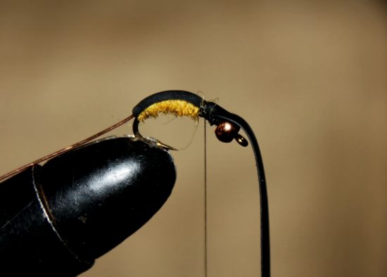 Dra litt i tapen, og dra den over ryggen på flua, og fest den med et par tighte tørn foran dubbingkroppen. Foto: Lasse Bøe